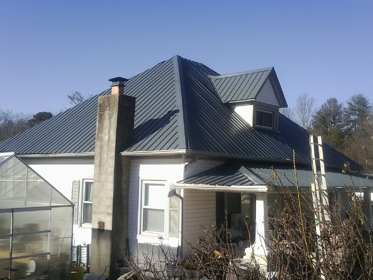 Dark blue standing seam metal roof on a white farmhouse with dormer — Slate & Tile Roof Repair by Roofing Brothers in Gracey
