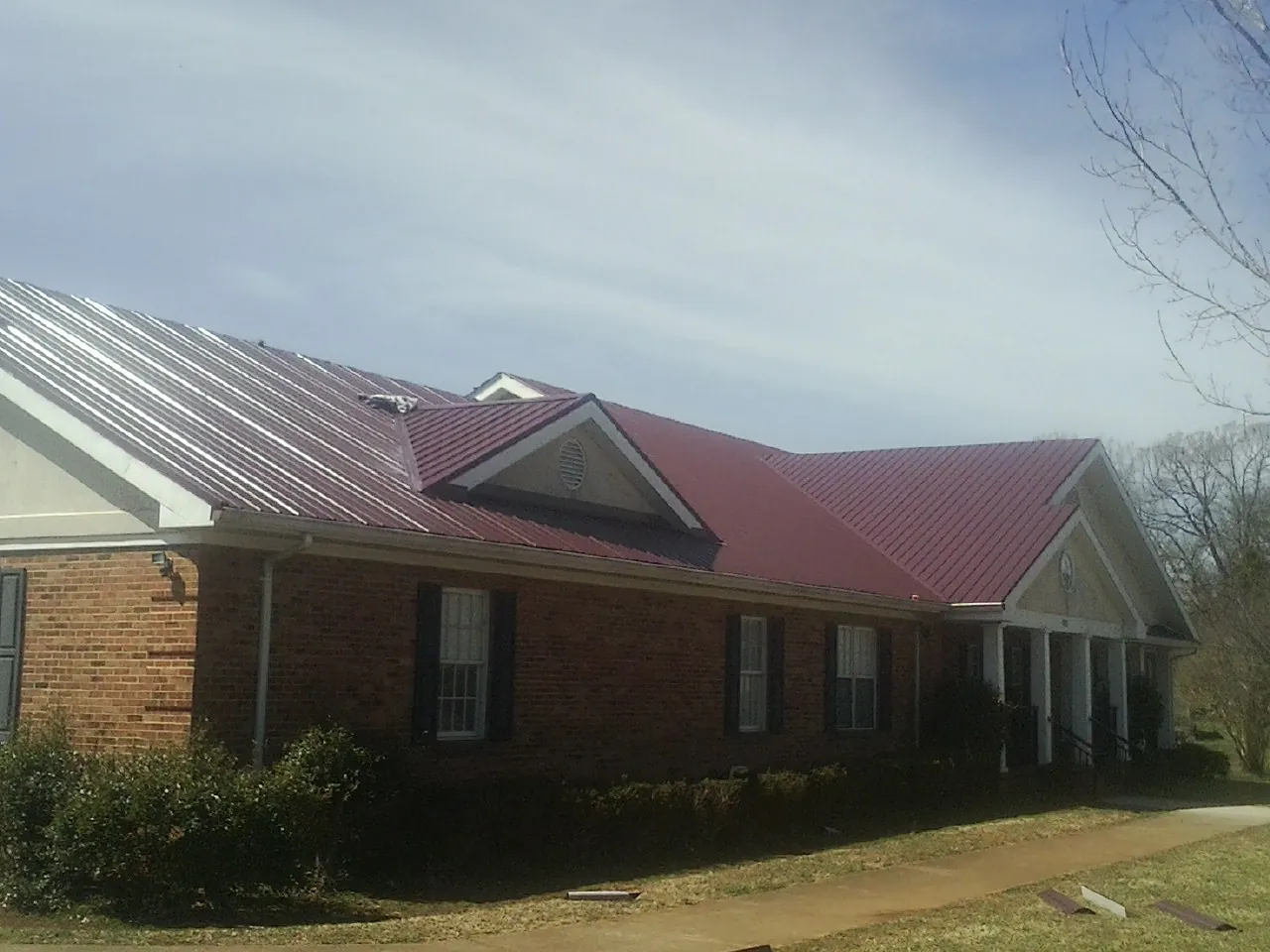 Red metal roof with gabled entries on a long brick building, from a Hail Damage Roof Repair job in Gracey