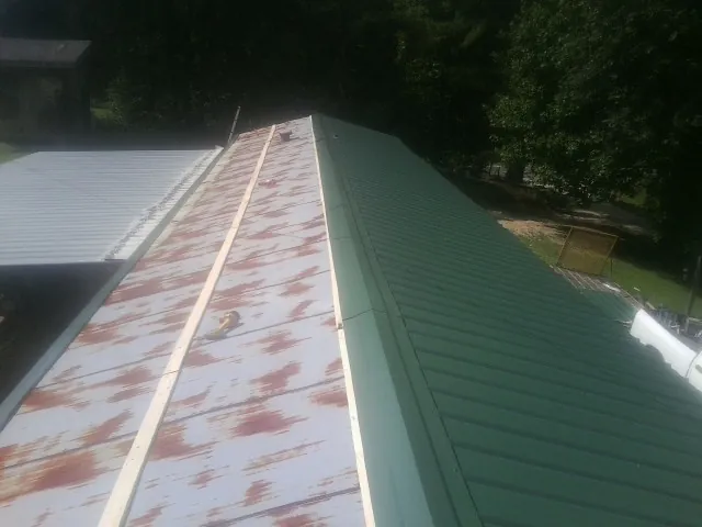 Old rusted panels beside newly installed green metal roofing — Wind Damage Roof Repair by Roofing Brothers in Gracey