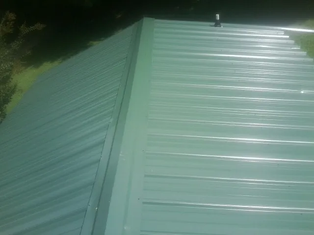 New green metal panels meeting at the ridge of a roof — Flat Roof Repair work by our crew in Gracey