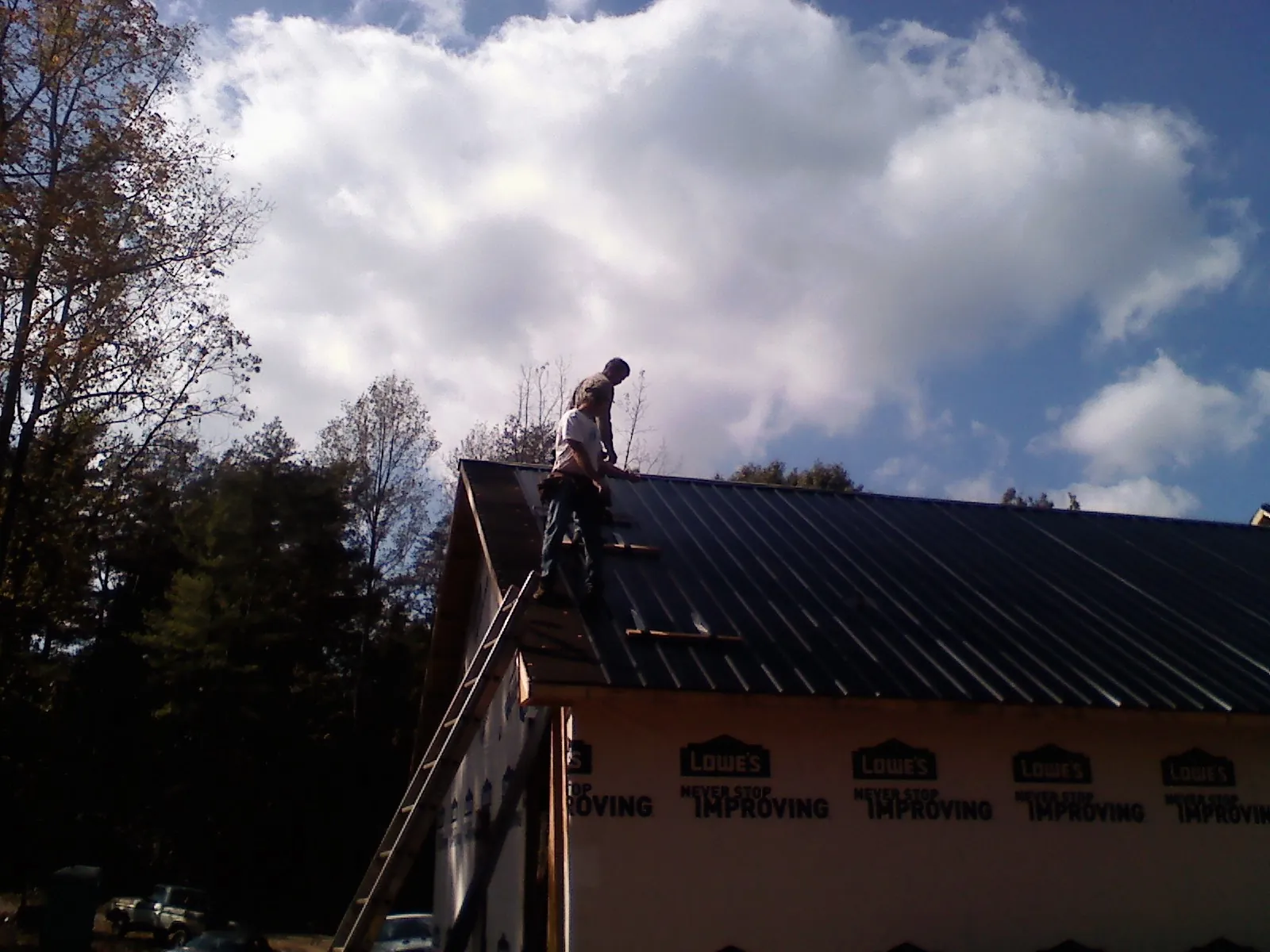 Roofer fastening dark metal panels high against a cloudy sky, from a Roof Inspection job in Gracey