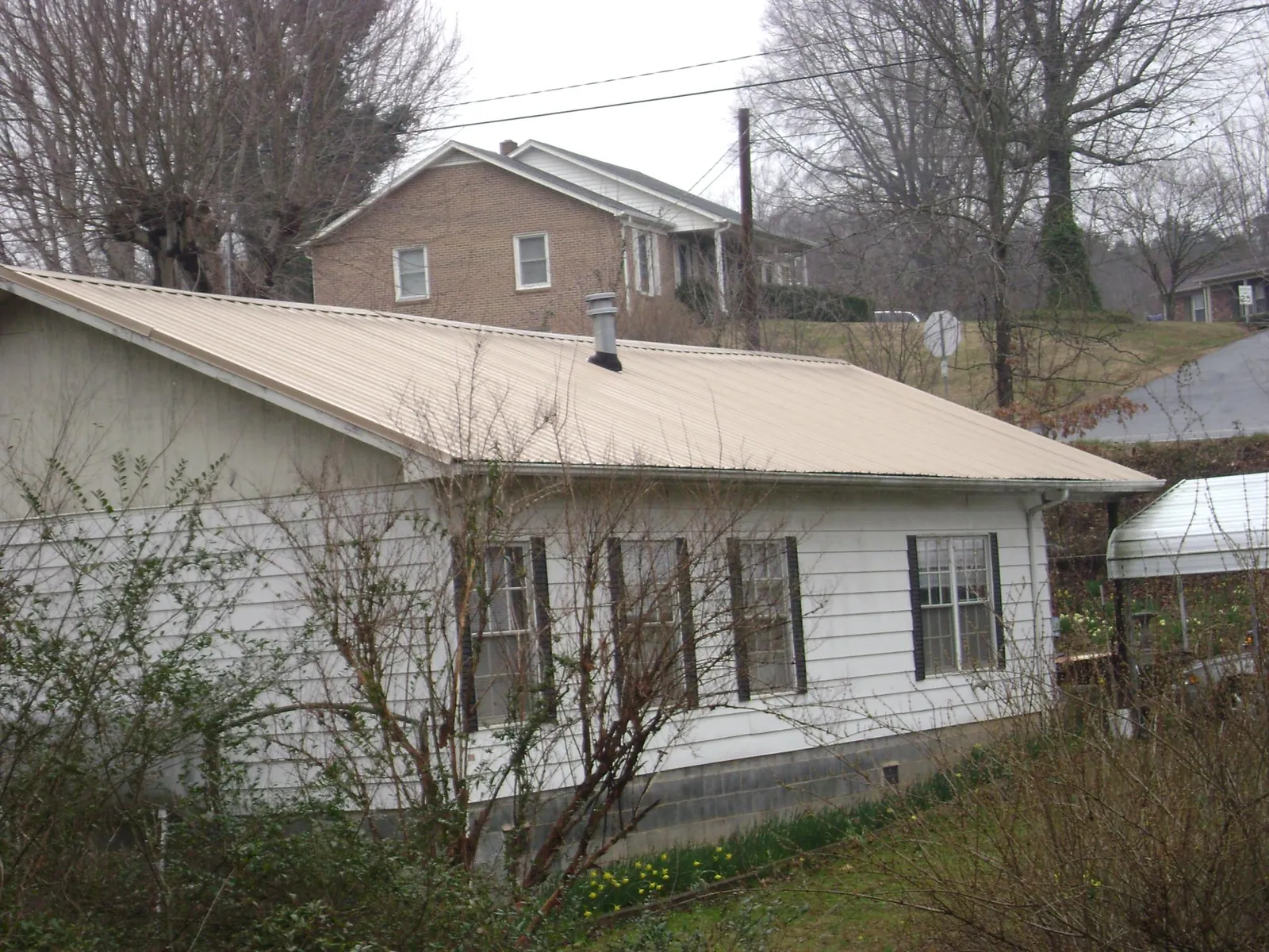 Tan metal roof on a white sided house set into a hillside — Commercial Roofing by Roofing Brothers in Gracey