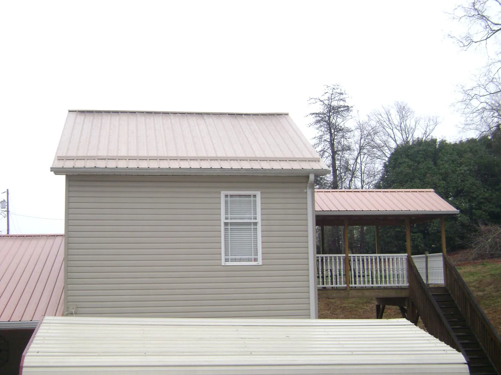 Tan metal roofs on a two story addition and attached porch, from a Roof Replacement job in Gracey